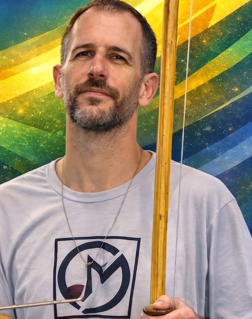 Instrutor Gigante segurando um berimbau, com a camiseta do grupo